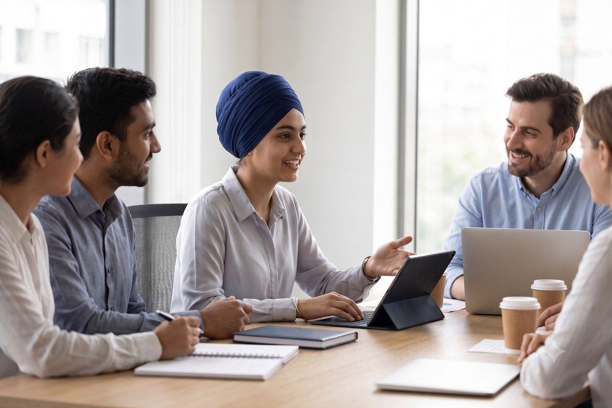 A young Sikh woman contributing in a workplace meeting alongside colleagues.